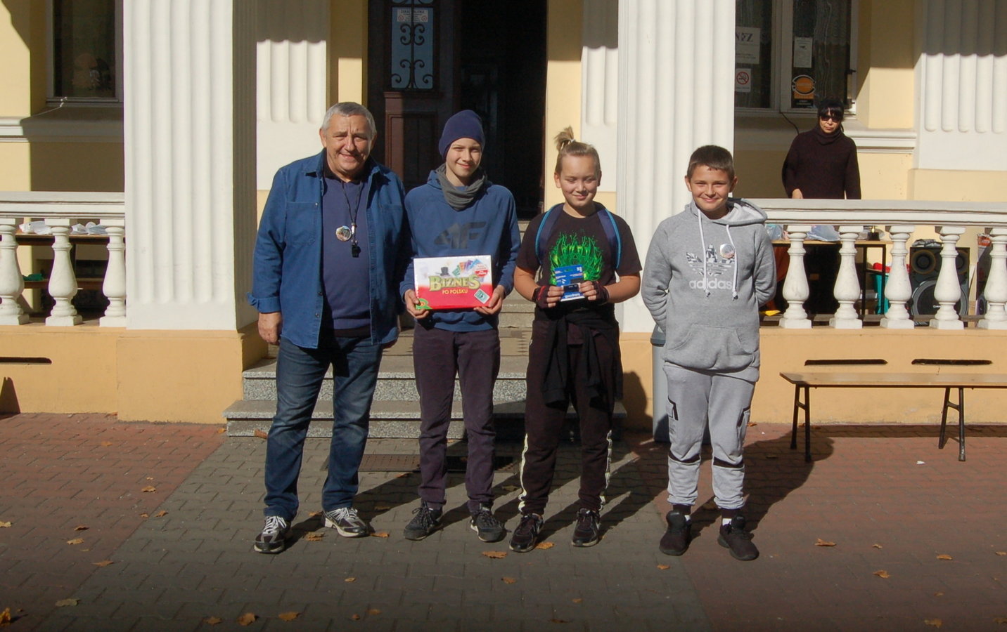 kierownik Ośrodka wraz z nagrodzonymi dziećmi i młodzieżą na tle wejścia do szkoły w Bronikowie